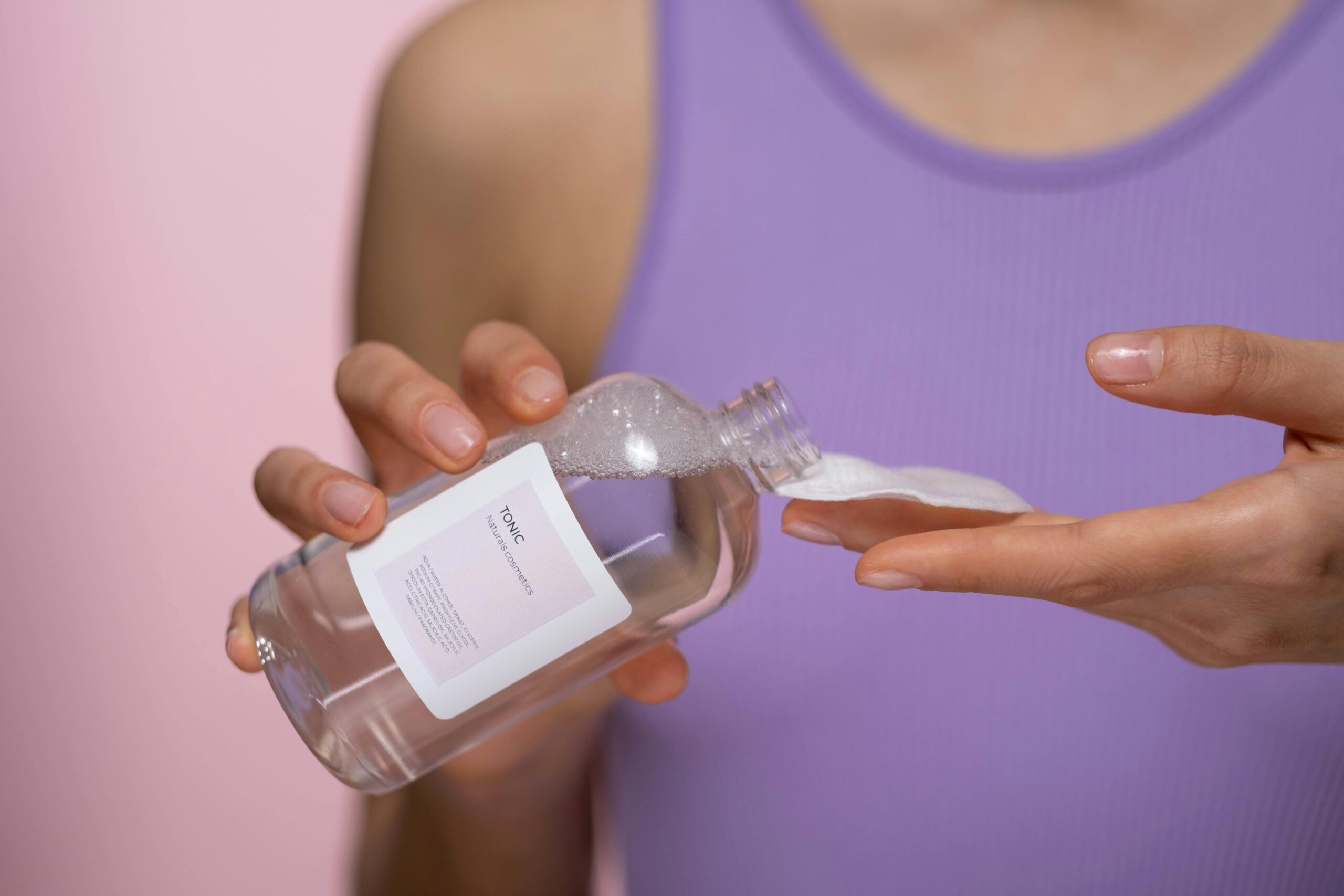 Home Woman applying skincare tonic with a cotton pad. Focus on hands and product in a studio setting.
